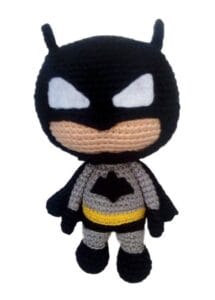 Muñeco Batman amigurumi tejido a crochet con traje gris, capa y máscara negra, cinturón amarillo y ojos blancos, sobre fondo blanco.