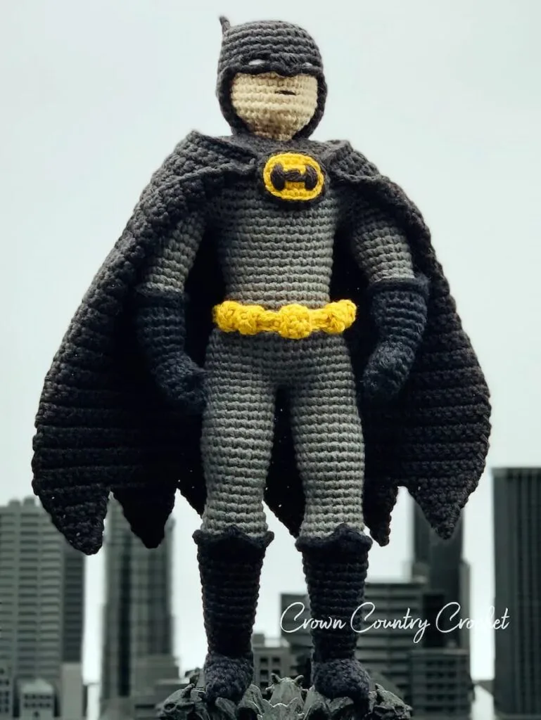 batman amigurumi en tamaño grande con capa negraa posano sobre terraza observando la ciudad