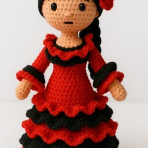 "Muñeca amigurumi vestida de flamenca, tejida a crochet con vestido rojo y negro de volados, cabello negro con flor roja, sobre fondo blanco."