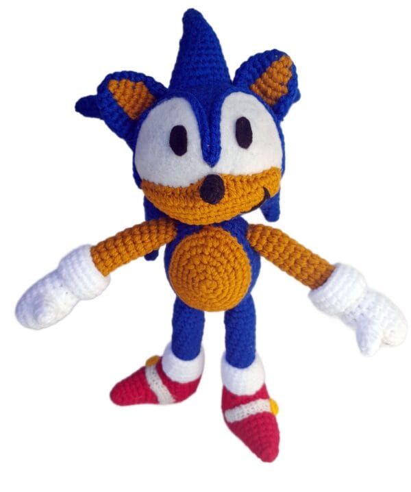 Amigurumi de Sonic tejido a crochet, vista frontal, mostrando su expresión decidida, ojos grandes y zapatillas rojas características, sobre fondo blanco.