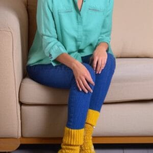 Una mujer morena sentada en un sofá beige con los pies juntos, luciendo unos zapatos tejidos a crochet de color amarillo pastel.