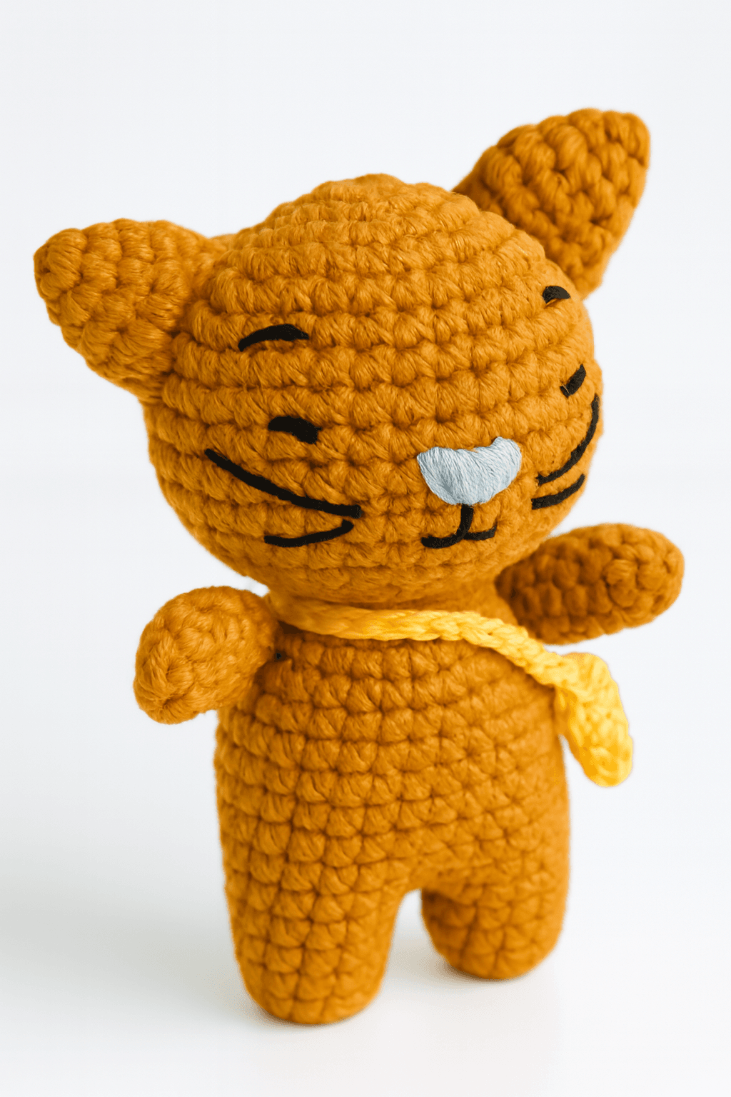 Patrón gratis de gatito amigurumi tejido en hilo naranja, con nariz blanca, ojos y bigotes bordados, y bufanda amarilla, de estilo tierno y hecho a mano